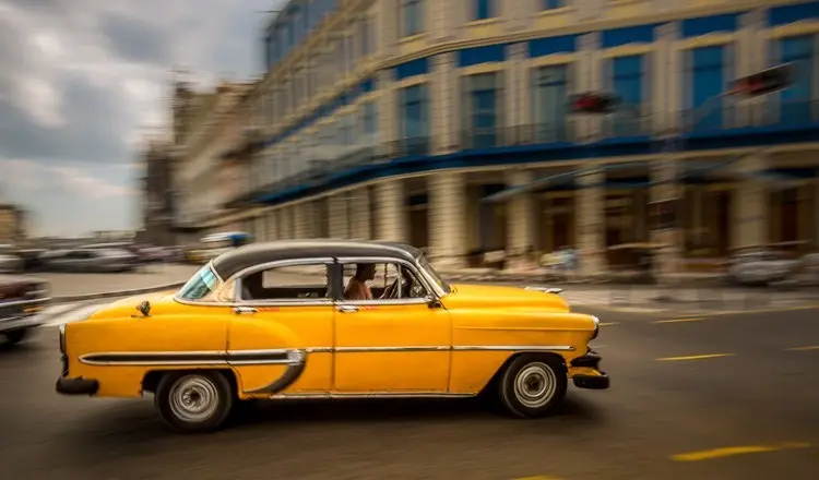 Carro fotografado com a técnica de panning: velocidade do obturador lenta mantém o carro nítido e transforma o fundo em linhas de movimento