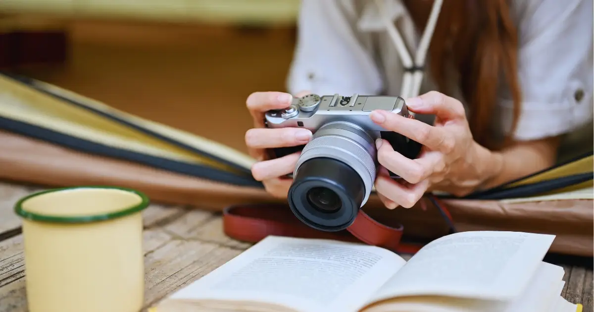 Pessoa folheando livros de fotografia ao lado de uma c&acirc;mera sobre a mesa